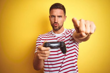 Genç yakışıklı adam video oyunları oynuyor sarı arka plan üzerinde oyun kağıtlarını kullanarak kamerayı işaret ediyor ve sen, el işareti, ön taraftan pozitif ve kendinden emin bir hareket.