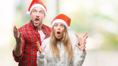 Üzerinde Noel şapka aşık genç çift çılgın kutlama arka plan izole ve başarı için kaldırdı kollarını açarak hayrete ve heyecanlı çığlık gözleri açık. Kazanan kavramı
