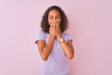 Genç Brezilyalı kadın pembe arka planda dikilip gülüyor ve utanıyor kıkırdıyor elleri, dedikoduları ve skandalları ağızlarına tıkıyor.