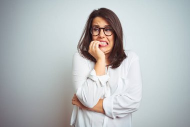 Stresli ve gergin elle çivi ısırma ağzına bakarak izole arka plan üzerinde gözlük takan genç güzel iş kadını. Anksiyete sorunu.