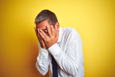 Yakışıklı orta yaşlı işadamı, izole edilmiş sarı arka planda duruyor. Ağlarken suratını ellerle kapatıyor. Depresyon kavramı.
