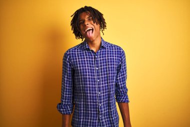 Rastgele tişörtlü Afro adam izole edilmiş sarı arka planda dikiliyor komik bir ifadeyle dilini dışarı çıkarıyor. Duygu kavramı.