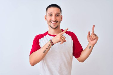 Genç yakışıklı adam izole edilmiş arka planda duruyor gülümsüyor ve kameraya bakıyor iki eliyle ve parmaklarıyla kenarı işaret ediyor..