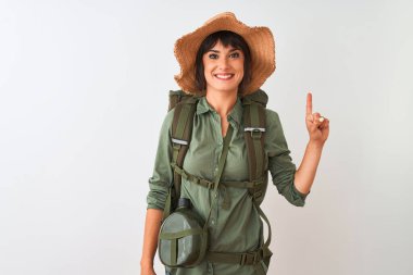 Sırt çantası şapkası ve su kantini takan yürüyüşçü kadın izole edilmiş beyaz arka plan üzerinde bir numaralı parmağını gösterirken kendine güvenen ve mutlu bir şekilde gülümsüyor..
