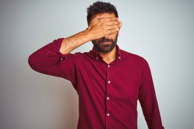 Kırmızı şık gömlek giyen genç Hintli adam, izole edilmiş gri arka planda duruyor, gözleri elle kaplıyor, ciddi ve üzgün görünüyor. Görme, saklama ve reddetme konsepti