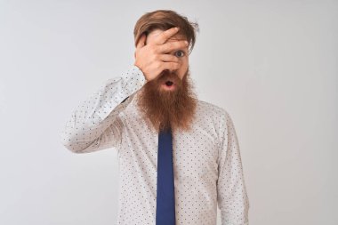 Genç kızıl saçlı İrlandalı işadamı, izole edilmiş beyaz arka planda dikiliyor. Şoka giriyor, yüzünü ve gözlerini eliyle kapatıyor, utangaç ifadesiyle parmaklarından bakıyor..