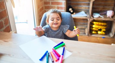 Anaokulunda renkli kalemlerle çizim yapan güzel bir çocuk.