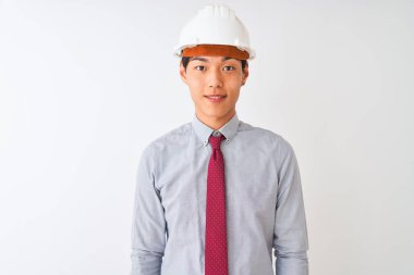 Yüzünde mutlu ve havalı bir gülümsemeyle izole edilmiş beyaz arka plan üzerinde duran kravat ve kask takan Çinli mimar. Şanslı kişi..