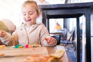 Güzel yürümeye başlayan çocuk kız masada oyuncaklar ile oynarken bebek mama sandalyesinde oturan