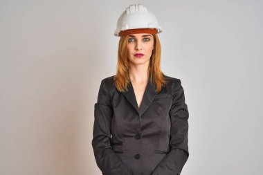 Kızıl saçlı beyaz iş kadını, izole edilmiş arka planda güvenlik kaskı takıyor ve yüzünde ciddi bir ifade var. Basit ve doğal bir şekilde kameraya bakıyorsun..
