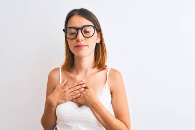 Güzel kızıl saçlı, gözlüklü, izole edilmiş arka planda gülümseyen elleri göğsünde, gözleri kapalı ve yüzünde minnet dolu bir jest olan bir kadın. Sağlık kavramı.