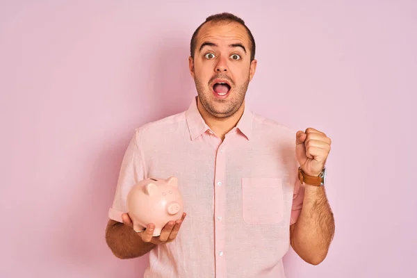 Joven Sosteniendo Piggybank Parado Sobre Fondo Rosa Aislado Gritando Orgulloso —  Fotos de Stock