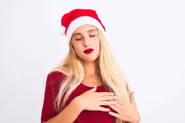 隔離された白い背景の上にクリスマスのサンタの帽子を身に着けている若い美しい女性は目を閉じて胸に手で笑顔と顔に感謝のジェスチャー 健康コンセプト — ストック写真