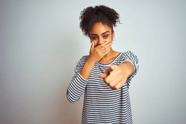 African american woman wearing navy striped t-shirt standing over isolated white background laughing at you, pointing finger to the camera with hand over mouth, shame expression