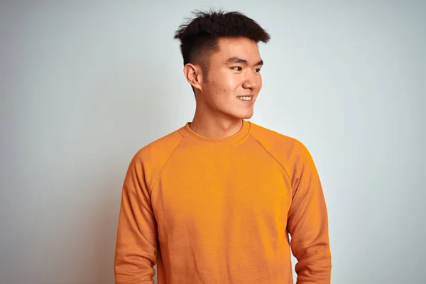 若いアジアの中国人男性の顔に笑顔で横に離れて見て孤立した白い背景の上に立ってオレンジ色のセーターを着て 自然な表情 自信を持って — ストック写真