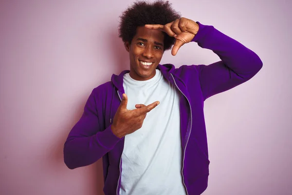 紫色のスウェットシャツを着た若いアフリカ系アメリカ人男性がピンクの背景に立って 手と指で幸せな顔でフレームを作って笑っています 創造性と写真の概念 — ストック写真