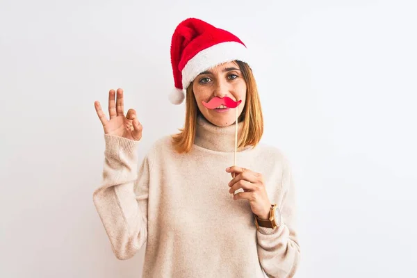 美しい赤毛女性身に着けていますクリスマスの帽子身に着けていますふり口ひげ上の隔離された背景を行います指でOkサイン 優れたシンボル — ストック写真