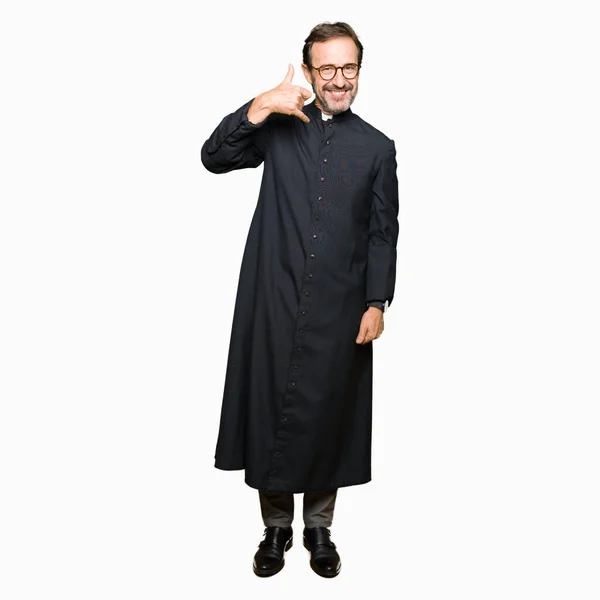 中年牧师男子穿着天主教长袍微笑着用手和手指做电话手势 就像在电话里说话一样 传达概念 — 图库照片
