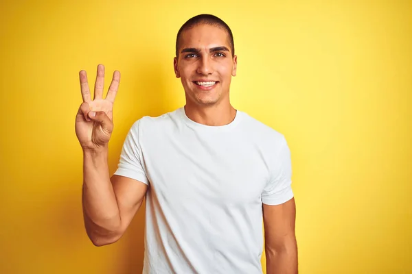 黄色の隔離された背景の上にカジュアルな白いTシャツを身に着けている若い白人男性が現れ 自信と幸せ笑顔ながら指の数3で指摘 — ストック写真