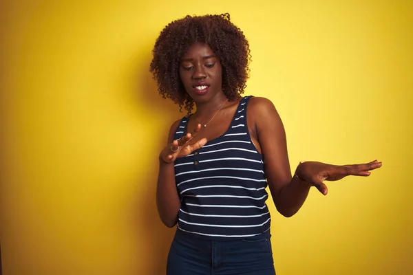 Young african afro woman wearing striped t-shirt over isolated yellow background disgusted expression, displeased and fearful doing disgust face because aversion reaction. With hands raised. Annoying concept.