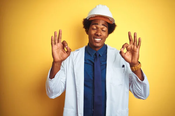 非洲裔美国工程师 身穿白色外套 头戴安全帽 头戴孤立的黄色背景 闭着眼睛 用手指做冥想手势 瑜伽概念 — 图库照片