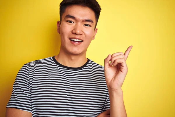 若いですアジアの中国人男性身に着けていますストライプTシャツ立って上の隔離された黄色の背景非常に幸せなポインティングで手と指で側面 — ストック写真