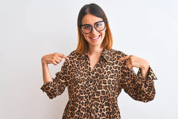 Beautiful redhead woman wearing glasses and elegant animal print shirt over isolated background looking confident with smile on face, pointing oneself with fingers proud and happy.