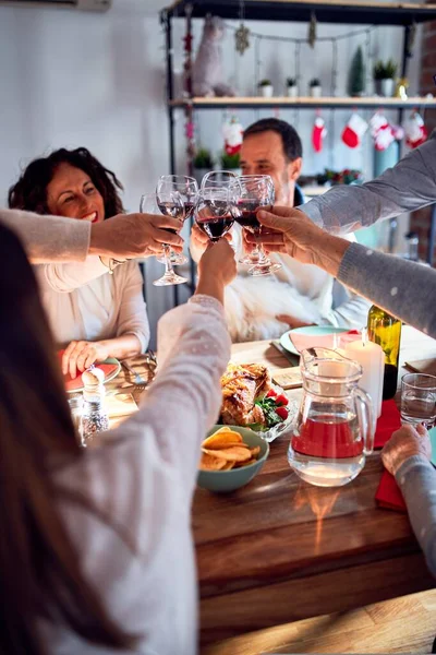 Family and friends dining at home celebrating christmas eve with traditional food and decoration, making a toast with best wishes with glass of wine