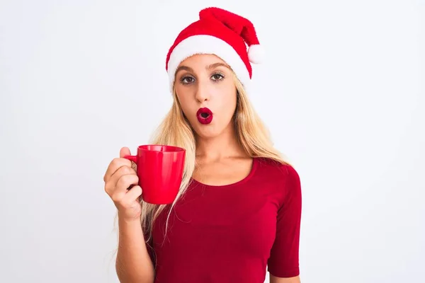 戴着圣诞圣诞礼帽的漂亮女人在与世隔绝的白色背景下喝咖啡 吓得满脸诧异 吓得面无血色 吓得面无血色 — 图库照片