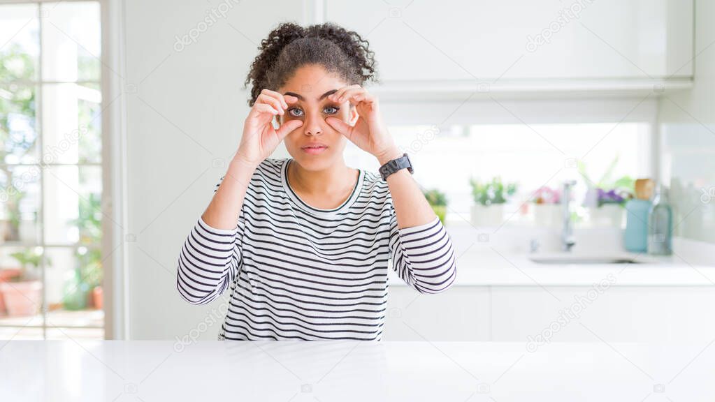 Beautiful african american woman with afro hair wearing casual striped sweater Trying to open eyes with fingers, sleepy and tired for morning fatigue