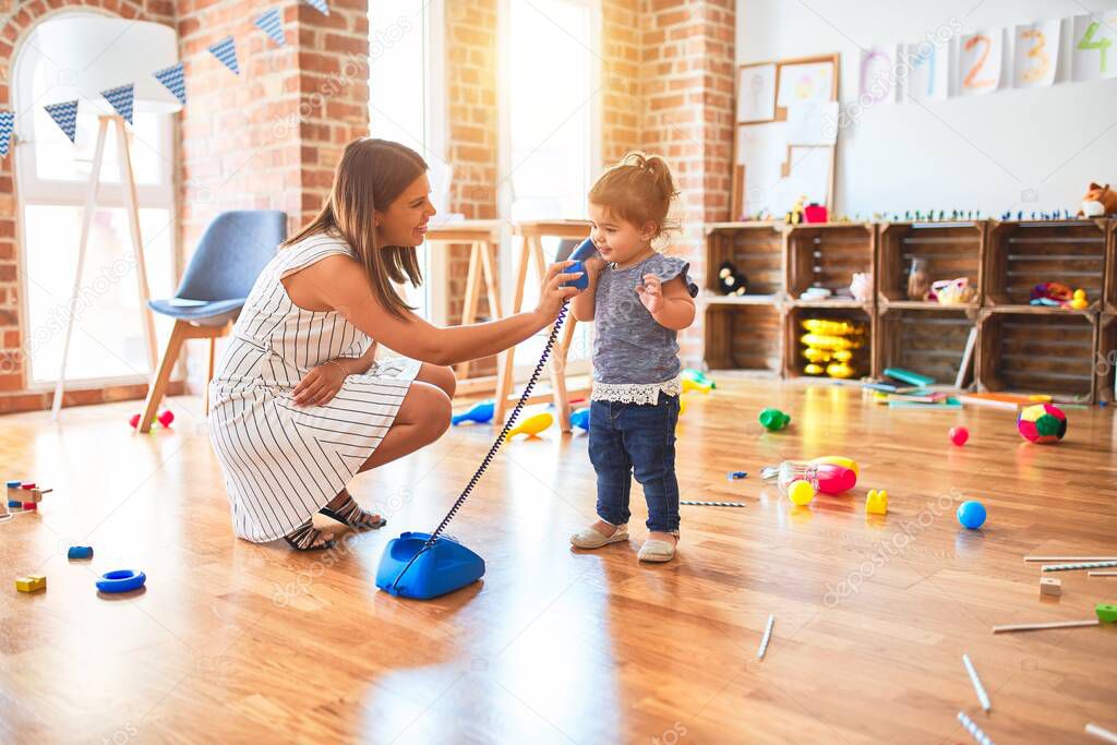 Young beautiful teacher and toddler playing with vintage phone at kindergarten