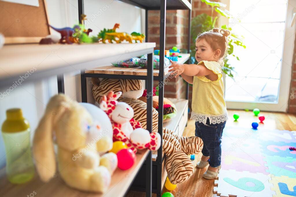 Beautiful toddler standing taking toys of shelving at kindergarten