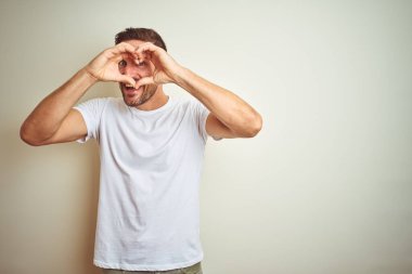 El ve parmak işareti seyir gülümseyen izole arka plan yapıyor kalp şekli üzerinde rahat beyaz t-shirt giyen genç yakışıklı adam