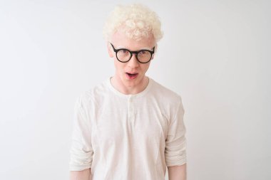 Genç albino tişört ve gözlük takan sarışın adam izole edilmiş beyaz arka planda korku dolu ve şaşkınlık dolu bir ifade, korku ve heyecanlı bir yüz ifadesiyle duruyor..