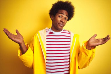 Siyah saçlı Afrikalı bir adam izole edilmiş sarı arka plan üzerinde duruyor. Kolları ve elleri havada, kafası karışmış bir ifade takınıyor. Şüphe kavramı.