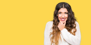 Emin çapraz kollar ve çeneme kaldırdı el ile gülümseme ile kameraya bakarak beyaz kazak giyen genç güzel kadın. Pozitif düşünce.