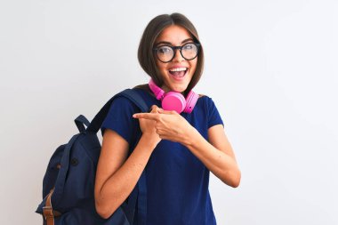 Sırt çantası gözlüklü genç bayan izole edilmiş beyaz arka planda kulaklık takıyor. El ve parmağıyla işaret ederek çok mutlu.