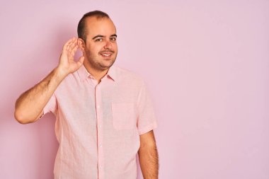 Soyutlanmış pembe arka planda duran zarif tişörtlü genç bir adam kulağına fısıldayarak dedikoduları ve dedikoduları dinliyor. Sağırlık kavramı.