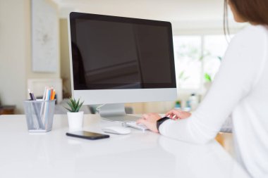 Bilgisayar kullanarak çalışan ve arka planda boş bir ekran gösteren gülümseyen genç kadın