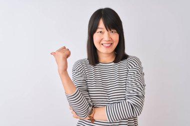 Genç, güzel Çinli bir kadın, izole edilmiş beyaz arka plan üzerinde siyah çizgili tişört giyiyor, gülümsüyor ve başparmağıyla yan tarafa bakıyor..