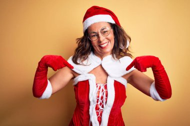 Orta yaşlı, güzel bir kadın. Noel Baba kostümü giyiyor. İzole edilmiş sarı arka planda..