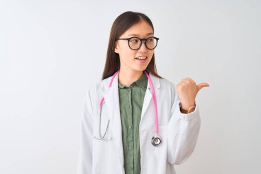 Genç Çinli kadın gözlüklü steteskop takıyor. İzole edilmiş beyaz arka planda gülümsüyor ve başparmağıyla yan tarafa bakıyor..