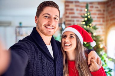 Mutlu ve kendinden emin gülümseyen genç bir çift. Evdeki Noel ağacının etrafında kamerayla selfie çekmek.