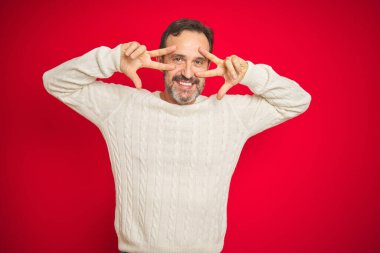 Yakışıklı orta yaşlı, gri saçlı, izole edilmiş kırmızı arka planda barış sembolü yapan, gülümseyen, zaferi gösteren bir adam.