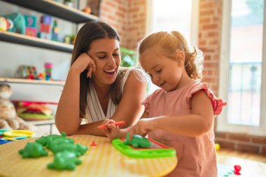 Güzel öğretmen ve sarışın kız çocuğu anaokulunda dijital tahta kullanarak resim çiziyor.
