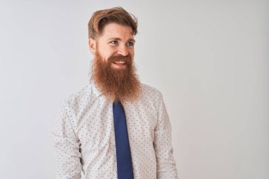 Genç kızıl saçlı İrlandalı işadamı, izole edilmiş beyaz arka planda duruyor. Yüzünde gülümseme, doğal bir ifade ile yan yana bakıyor. Kendinden emin gülen.