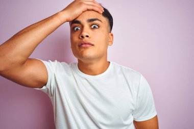 İzole edilmiş pembe arka planda dikilen Brezilyalı genç bir adam. Elleri başının üstünde, utanç ve şaşkınlık dolu, sinirli ve hayal kırıklığına uğramış bir halde. Hata için korku ve üzüntü.