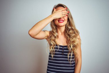 İzole edilmiş beyaz arka plan üzerinde duran çizgili tişört giyen genç ve güzel bir kadın. Gülümsüyor ve elleri yüzünde şaşkınlıktan gözleri kapatıyordu. Kör kavram.