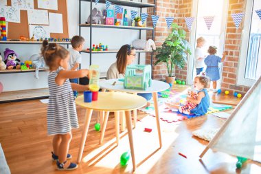 Güzel öğretmen ve bir grup çocuk anaokulunda bir sürü oyuncakla oynuyorlar.