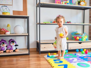 Renkli oyun odasında beyaz güzel bir bebek oyuncaklarla oynuyor. Anaokulunda mutlu ve neşeli renkli balolar..